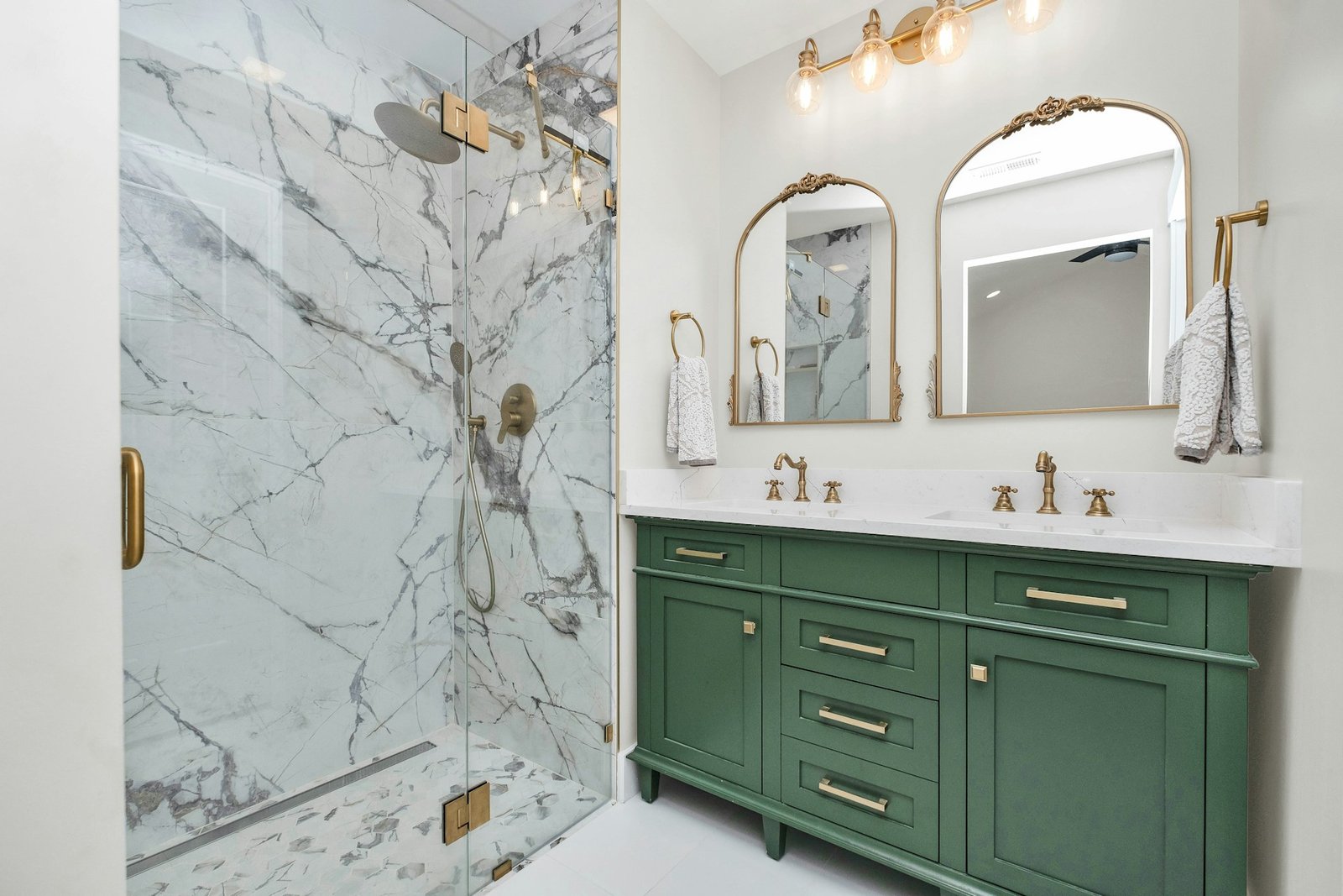 Remodeled bathroom with green vanity cabinets and a marble-tiled walk-in shower
