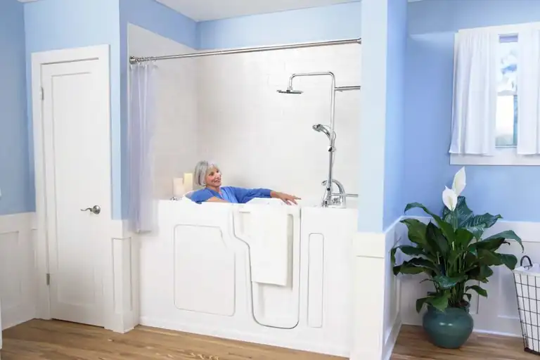 Woman relaxing in a white SafeStep walk-in tub with a built-in seat, outward-opening door, and handheld shower
