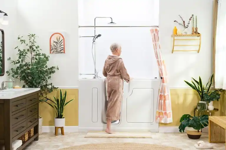 Senior woman in a robe stepping through the open door of a SafeStep walk-in tub